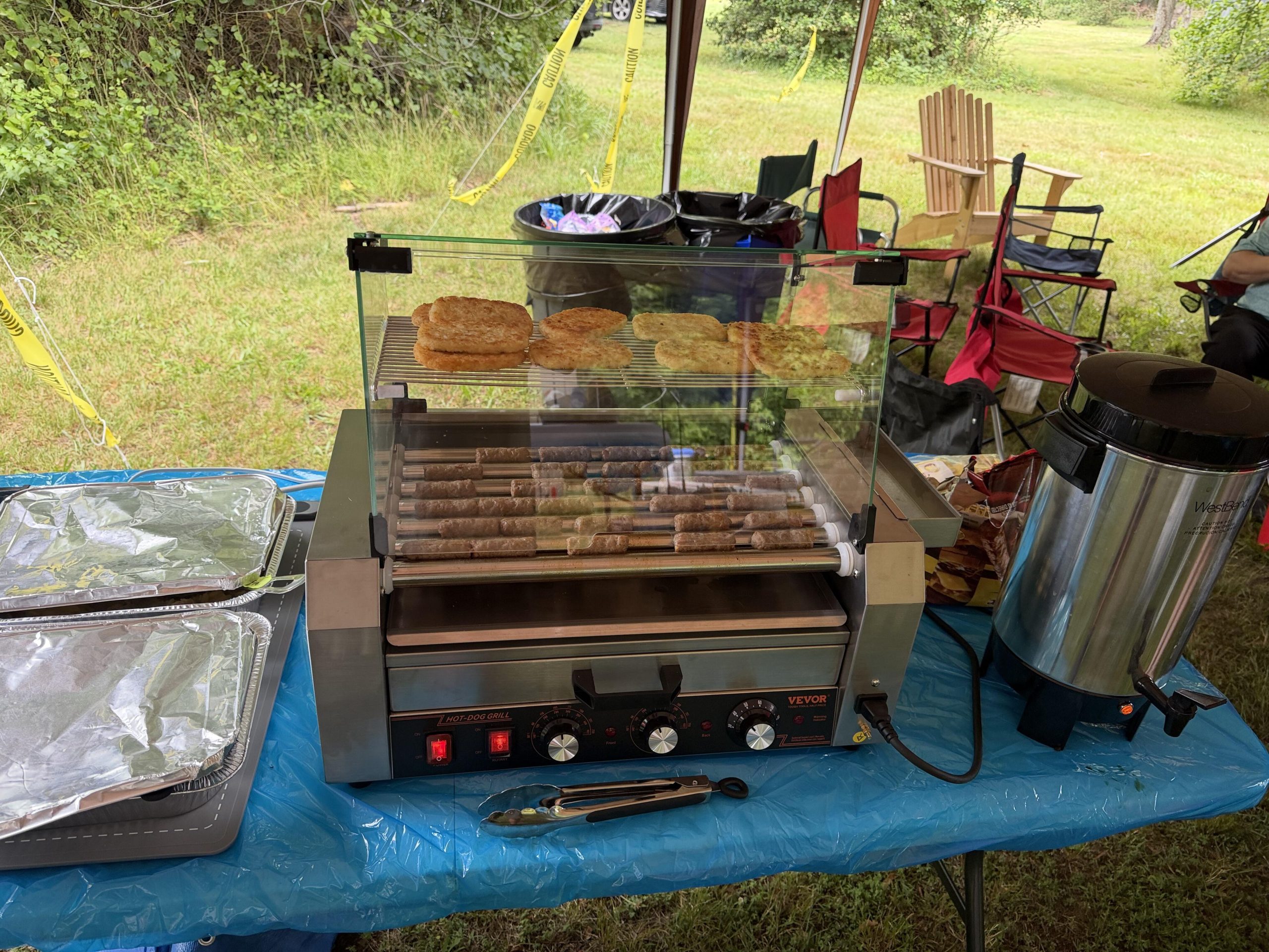 VEVOR hot dog roller with breakfast sausage links and hash browns warming on top rack, West Bend coffee urn at right