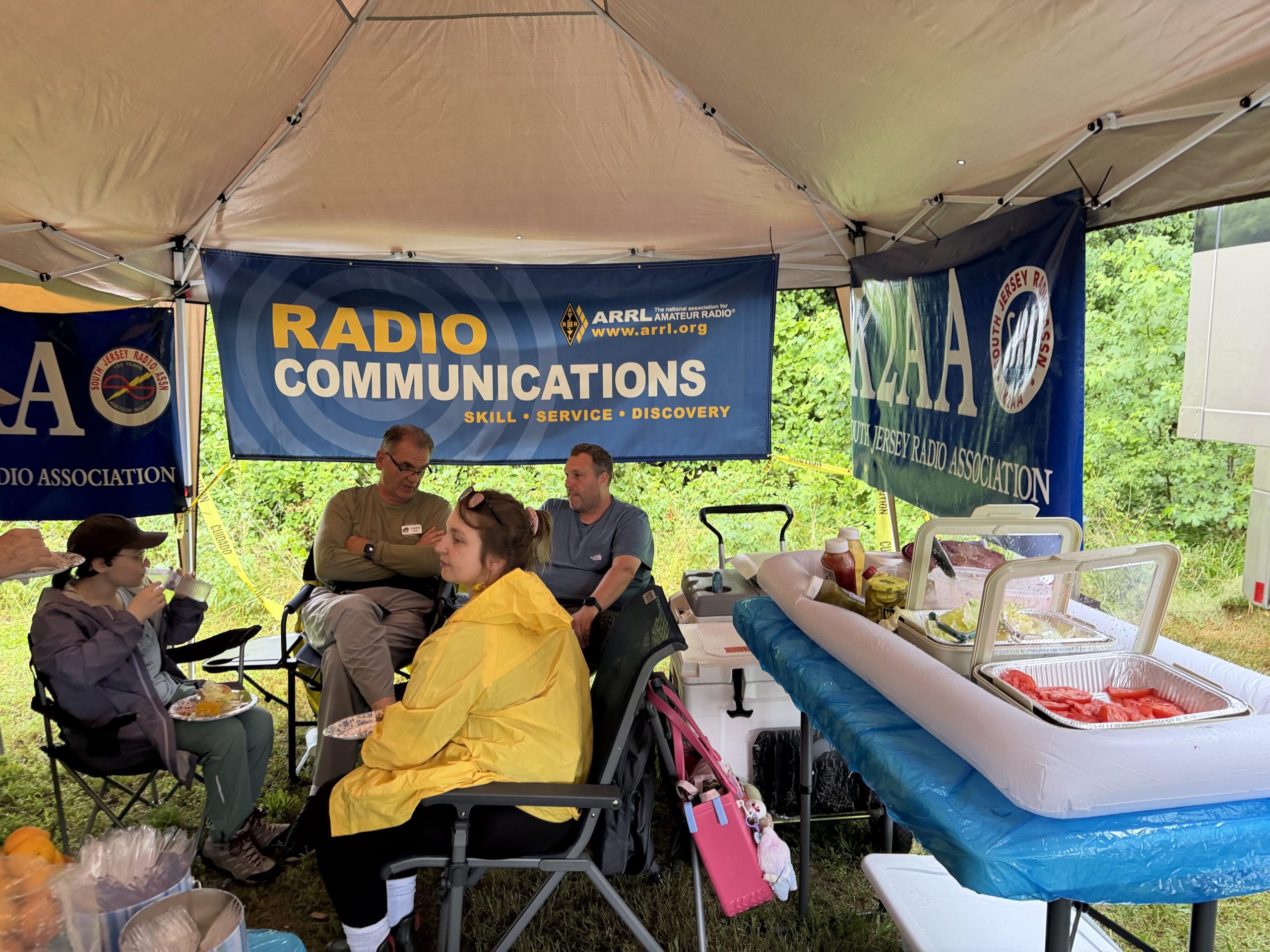 SJRA hospitality tent interior with ARRL Radio Communications banner and guests seated