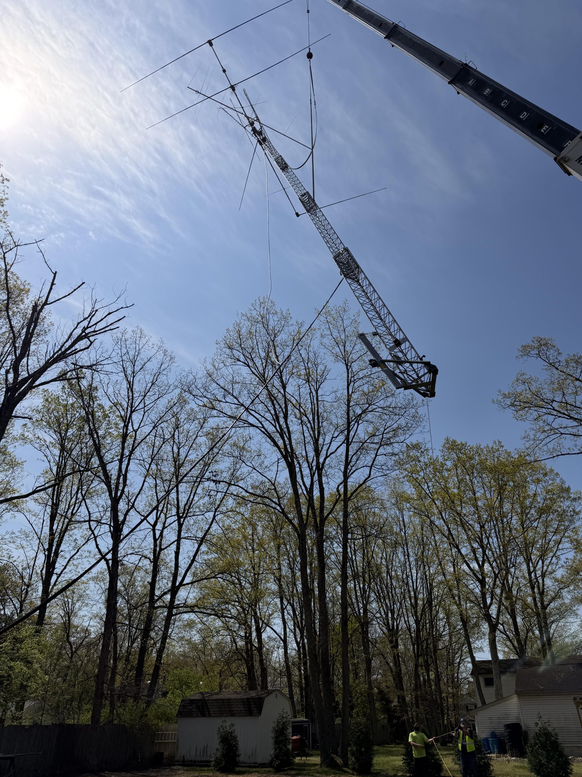 Antenna array suspended from the crane boom, clear of the tree canopy against blue sky