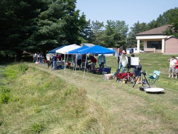 Line of MDS competition stations under canopies along a grassy hillside